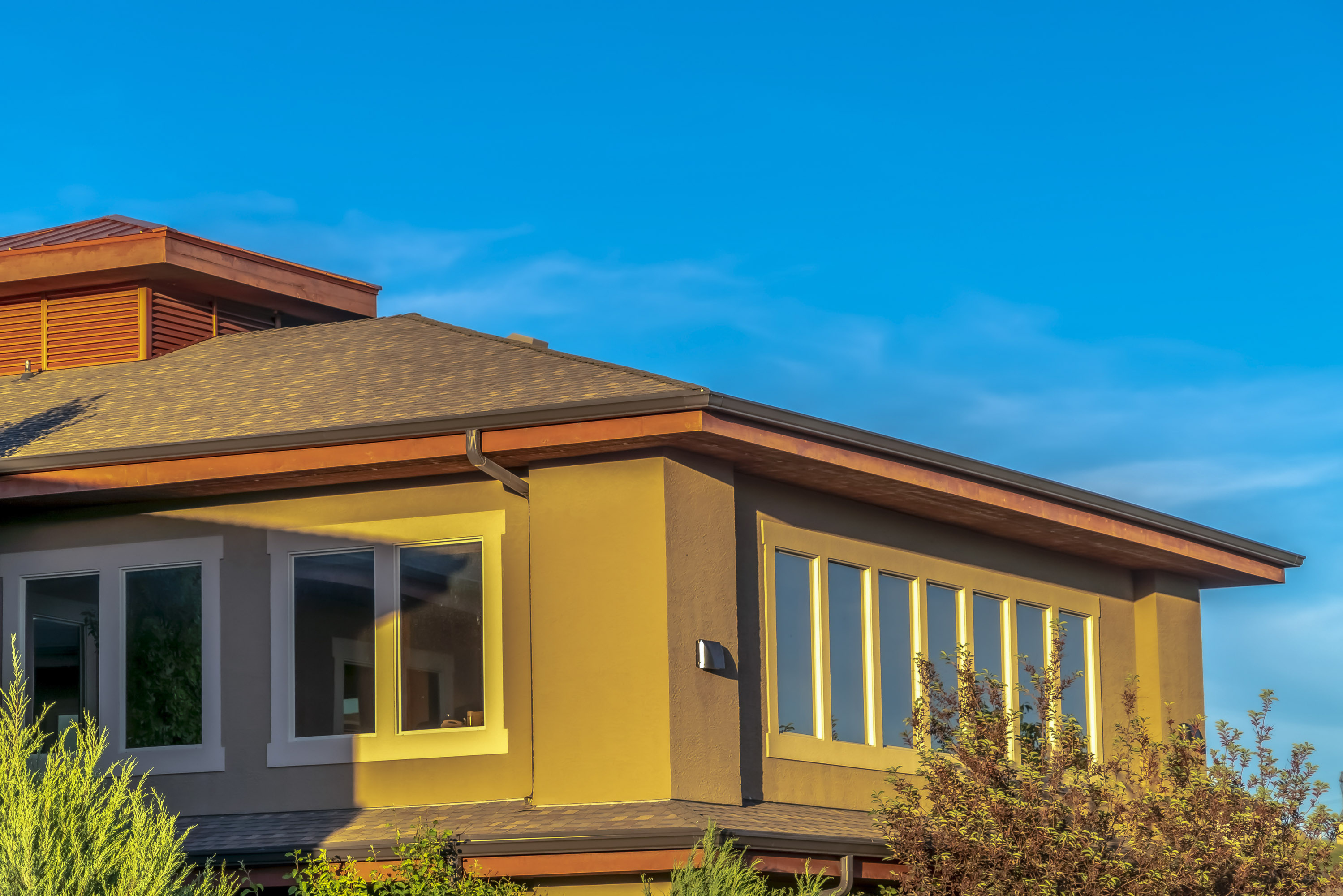 Brown home with a shingled hip roof against a bright blue sky